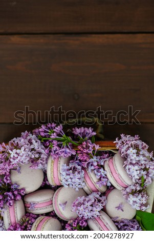 Macaroni cakes lying in lilac flowers on a wooden background. Place for text 