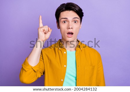 Photo of impressed brunet millennial guy point up wear yellow shirt isolated on violet color background