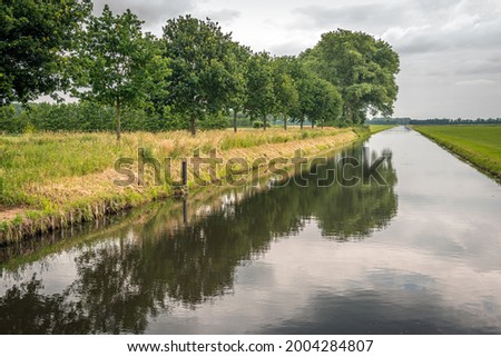 Dutch drainage canal Koningsvliet on a cloudy and windless day in the beginning of the summer season. The photo was taken at the village of Elshout, municipality of Heusden, province of North Brabant.