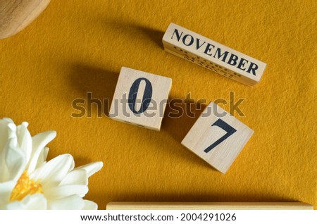November 7, Wooden Calendar cube on yellow felt fabric with peony flower for date icon background.