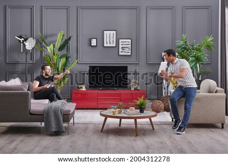 Two man spending time at home, decorative grey wall background and watching television style.