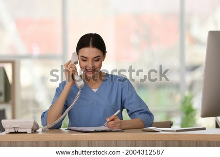 Receptionist talking on phone at countertop in hospital Royalty-Free Stock Photo #2004312587
