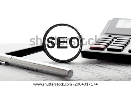 Magnifying glass with text SEO on the chart with pen and calculator