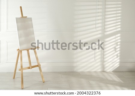 Wooden easel with blank canvas near light wall. Space for text