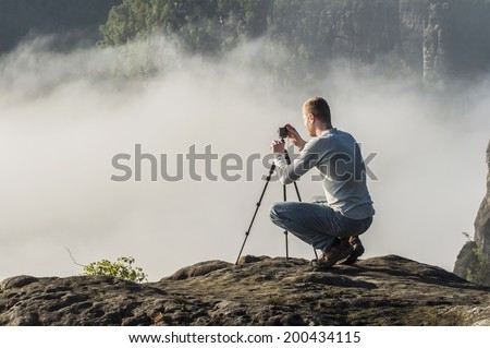 Photographer with the tripod on the sandstone rock in misty national park Saxon Switzerland 
