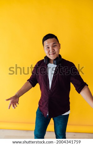 Asian man dances to music with headphones on a yellow background