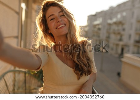 Portrait of well-groomed woman with gorgeous smile with teeth and long hair against the backdrop of city. Takes selfie while standing on her summer terrace. Royalty-Free Stock Photo #2004352760