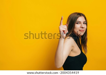 oung brunette woman pointing finger up and smiling, copy space. isolated over yellow background.	