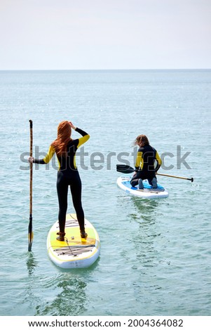 Young woman and man paddling on SUP board at sea at sunny day. Stand up paddle boarding is awesome active recreation in nature. Copy Space. Vacation, summer, sport, healthy lifestyle concept