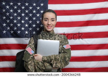 Female soldier with backpack and laptop near flag of United States. Military education