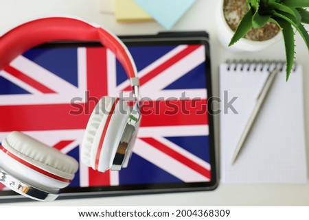 Tablet with image of British flag with headphones and notebook with pen lie on table