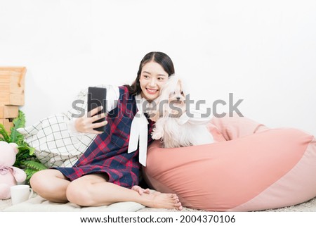 Asian woman takes a selfie with a small dog. A woman takes a selfie as she holds her Maltese dog.