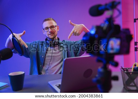 The blogger points his fingers down so that viewers will pay attention to the pop-up "subscribe"icon. A vlogger needs to attract as many followers as possible to his channel. Royalty-Free Stock Photo #2004383861