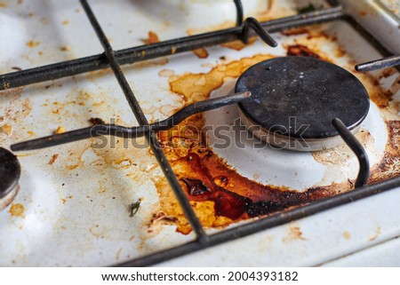 Dirty stove with food leftovers. Unclean gas kitchen cooktop with greasy spots, old fat stains, fry spots and oil splatters. Royalty-Free Stock Photo #2004393182