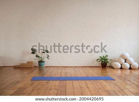 Yoga mat lying on wood floor in a yoga studio. Yoga studio decorated with sport's equipment and tropical plants. Royalty-Free Stock Photo #2004420695