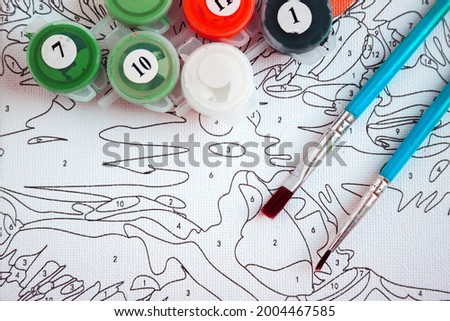 Acrylic paints in jars and brushes of two types on canvas with markings - painting by numbers, hobbies
