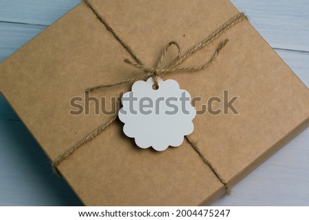 Gift box tied with a jute rope in rustic style, with a white tag, on a light wooden background, place to insert text and copy space