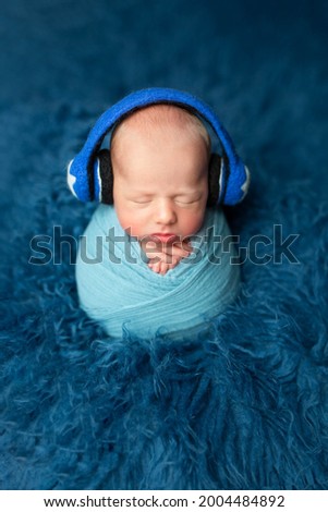 newborn baby in headphones on a blue background. the first photo session of the child. child photographer, musical baby