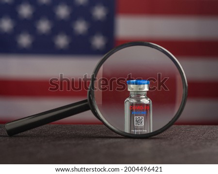 Magnifying glass at COVID-19 vaccine bottle with the American flag background.  Vaccine for immunization, and treatment from coronavirus infection. Close-up photo. Concept of medical and healthcare.