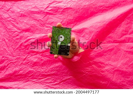 Hand holding 2.5 HDD through hole in pink rumpled paper. Mining 
