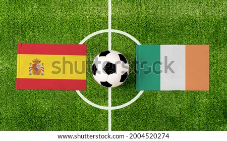Top view soccer ball with Spain vs. Ireland flags match on green football field.