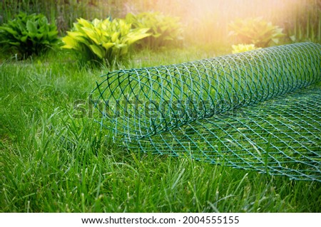 roll of plastic green mesh for the garden lies on the lawn. garden net for fixing plants and fencing is ready for work