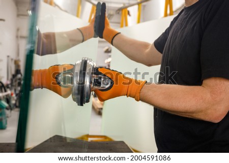 Glazier holding a thick pane of glass with a suction cup, Glass Factory, Specialist work tools  Royalty-Free Stock Photo #2004591086