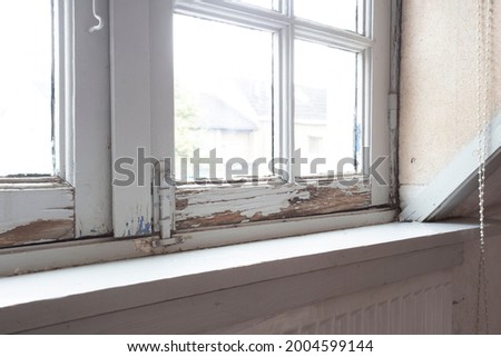 Old wooden window frames with rotting wood and cracked peeling paint, house needs renovation and new frames closeup Royalty-Free Stock Photo #2004599144