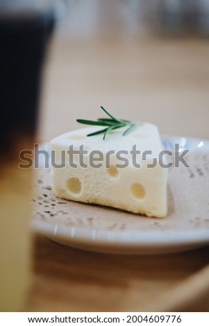 Closed up picture of a small white cheese shaped cheesecake on a delicate plate topped with rosemary leaves
