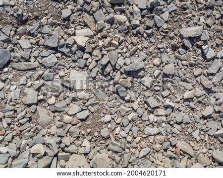 The texture of uneven roughly split gray small stones in close-up. The background of rubble in full screen.