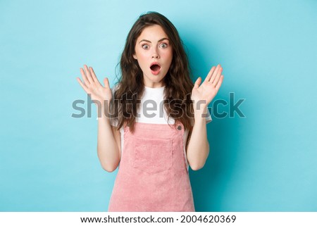 Portrait of shocked attractive woman gasping, spread hands sideways and stare startled at camera, hear worrying terrible news, looking with disbelief, standing against bue background Royalty-Free Stock Photo #2004620369