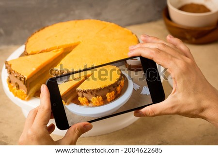 Female Hands with phone taking pictures of Halloween cake. Pastry cook filming video blog.