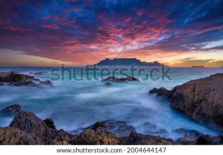 Beautiful sunset sky above a wispy long-exposure sea. Table Mountain sets the backdrop for a vibrant and colourful panorama Royalty-Free Stock Photo #2004644147