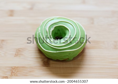 Close-up picture of a donut covered with green cream, isolated on wooden table.