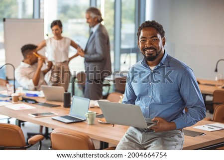 Mature black businessman with colleagues sitting in a modern board room. Proud smiling business man sitting during a meeting and looking at camera. Portrait of happy successful executive with team  Royalty-Free Stock Photo #2004664754