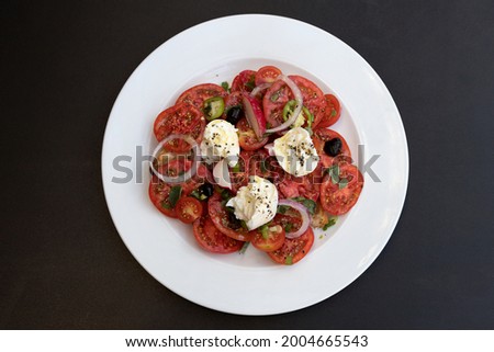 Italian caprese salad with chopped tomatoes, mozzarella, basil, oregano, thassos, onions, radishes, chili peppers and olive oil on a white plate.