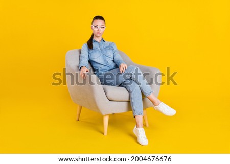 Photo of serious confident young woman wear denim shirt glasses sitting chair isolated yellow color background