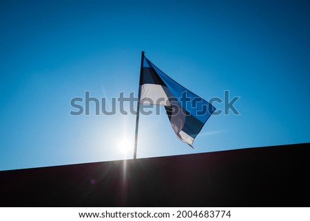 Estonian flag waving in wind and sunlight. Flag of Estonia on blue sky background.