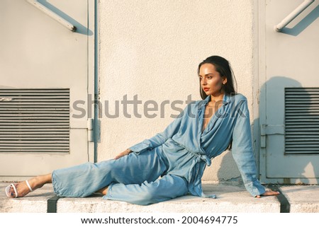
a girl in a blue jumpsuit poses on the street. brunette in a blue suit on the street on a sunny day Royalty-Free Stock Photo #2004694775
