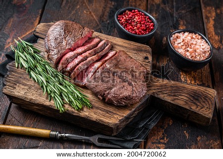 Fried Top Blade or flat iron roast beef meat steaks on wooden board with rosemary. Dark wooden background. Top View Royalty-Free Stock Photo #2004720062
