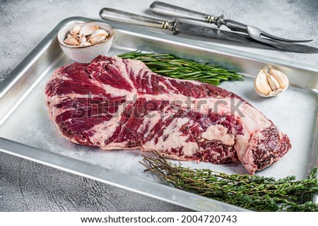 Raw hanger or onglet beef meat steak in steel tray with herbs. White background. Top View