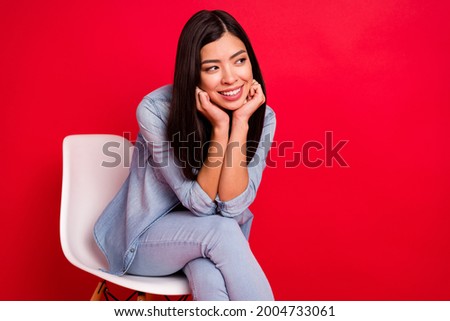 Portrait of attractive cheerful girl sitting in chair thinking looking aside copy space isolated over bright red color background