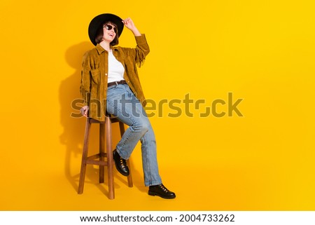 Photo of shiny funky young lady wear cowgirl outfit dark glasses headwear sitting bar chair empty space isolated yellow color background Royalty-Free Stock Photo #2004733262