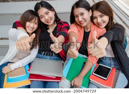Group of four young attractive asian girls college students smiling to camera doing thumbs up in university campus outdoor. Concept for education, friendship and college students life.