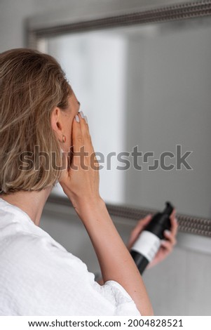 Beautiful blonde girl in white bathrobe doing morning routine by the mirror holding plastic package with white sticker