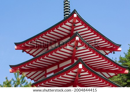 The bright red pagoda temple against the blue sky surrounded by the nature of the mountain forest decorated with bright pink cherry blossoms perfectly reflects the architecture and culture of Japan.