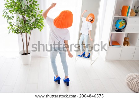 Photo of cute funny small schoolgirl dressed white t-shirt wearing moms shoes dress looking mirror indoors room home house