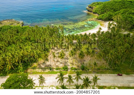 Drone picture in pacifico in siargao, philippines, with a road and a car in the foreground, a land full of coconut trees in the middle, a beach and the sea in the background