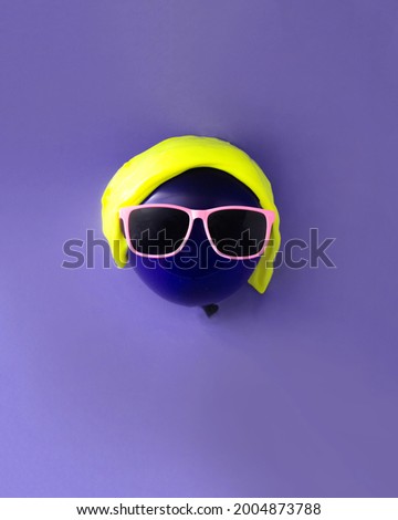 Purple balloon with yellow slime and pink glasses. Purple background. Minimalism.