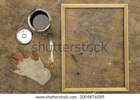 There are wooden frame and some things on old scratched table. On the photo we can see work place. In this place some human painted frame for photo.	

